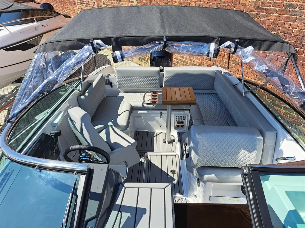 A spacious boat interior with plush seating, a wooden table, and clear canopy, featuring a modern design and gray upholstery.